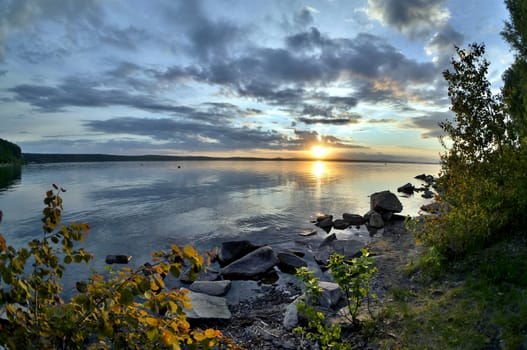 the evening sky over the lake, silhouettes of clouds illuminated by the sun, forest-covered shore of the lake