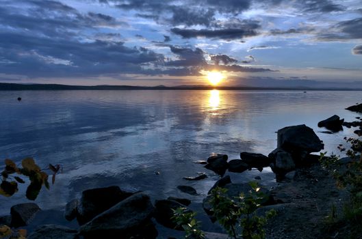 the evening sky over the lake, silhouettes of clouds illuminated by the sun