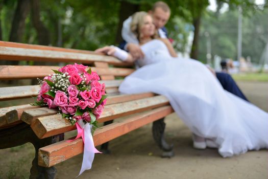 bouquet on wooden bench with bride and groom in the background, focus on the flowers. flowers on the background of the newlyweds