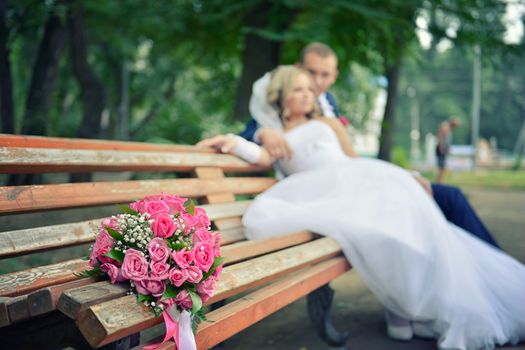 bouquet on wooden bench with bride and groom in the background, focus on the flowers. flowers on the background of the newlyweds