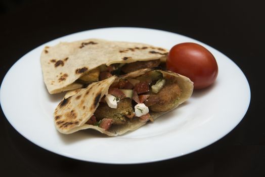 Pita bread filled with falafel and salad isolated on black.