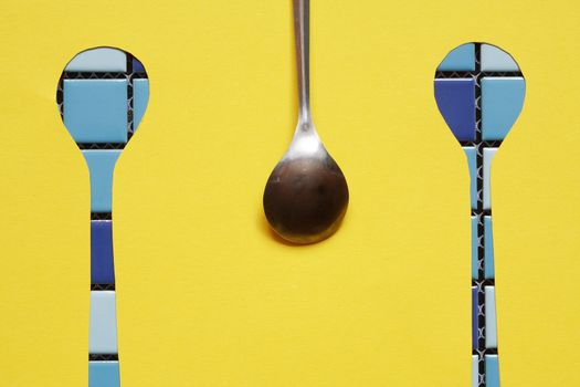 Abstract concept. One metal spoon with two spoons gap against yellow paper