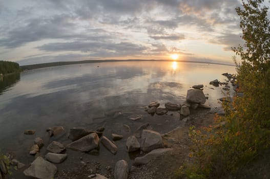 the evening sky over the lake, silhouettes of clouds illuminated by the sun, forest-covered shore of the lake