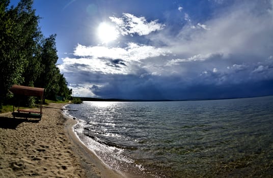 dark blue sky over the lake before the storm, the sun is shining