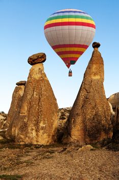 Hot air baloon flying over spectacular stone cliffs in Cappadocia near Goreme, Turkey