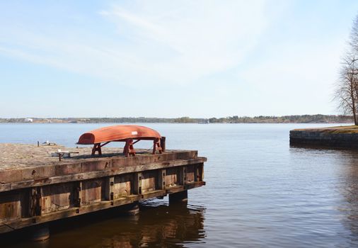 Upturned red boat on a pier above still water on the shore of Suomenlinna sea fortress in Finland