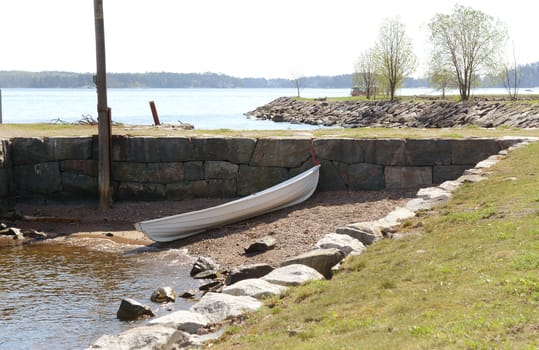 Small white rowboat on a small stony area of shore, against a stone wall on Suomenlinna island, Finland