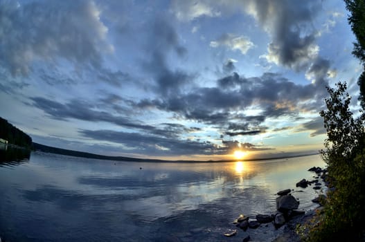 the evening sky over the lake, silhouettes of clouds illuminated by the sun, forest-covered shore of the lake