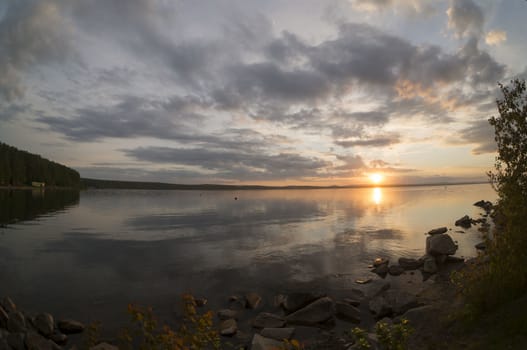 the evening sky over the lake, silhouettes of clouds illuminated by the sun, forest-covered shore of the lake