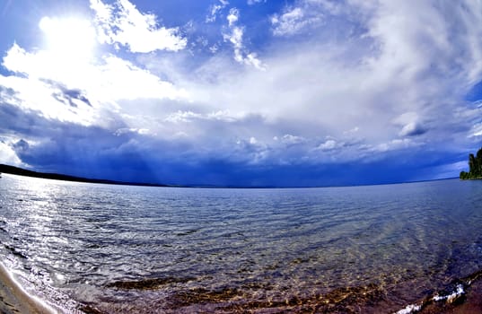 dark blue sky over the lake before the storm, the sun is shining