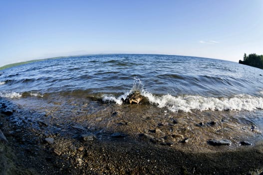 wave rages and runs on the shore of the lake on a bright Sunny morning, shooting from the bottom point