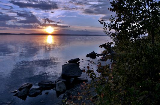 the evening sky over the lake, silhouettes of clouds illuminated by the sun