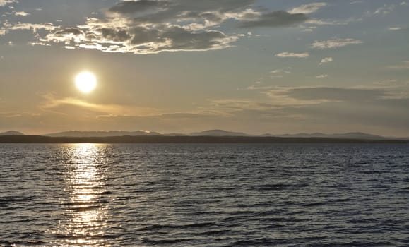 the evening sky over the lake, silhouettes of clouds illuminated by the sun