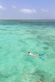 Woman snorkeling in clear shallow sea of tropical lagoon with turquoise blue water and coral reef, near exotic island. Mnemba island, Zanzibar, Tanzania.