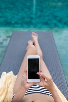 Woman relax on sunbath in swimming pool with using mobile phone