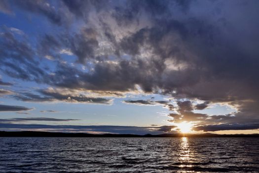 the evening sky over the lake, silhouettes of clouds illuminated by the sun