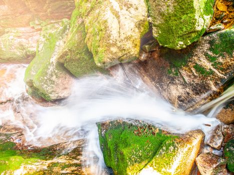 Water cascade of small creek between mossy stones. Long exposure