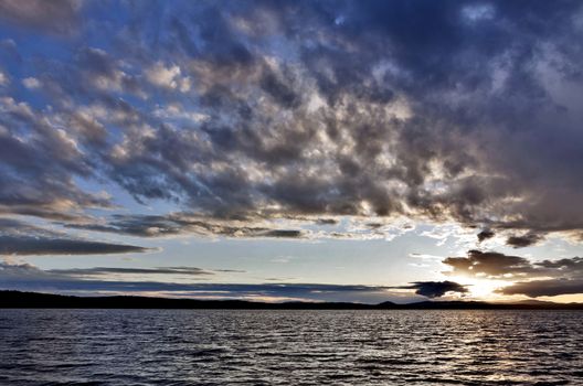 the evening sky over the lake, silhouettes of clouds illuminated by the sun