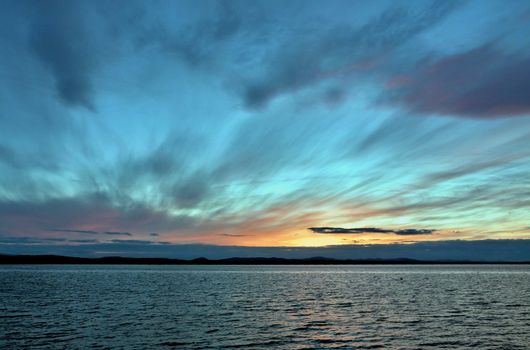 the evening sky over the lake, silhouettes of clouds illuminated by the sun, the sun sets over the horizon