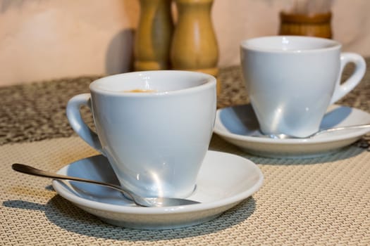 Composition of two cups of coffee on white serving plates with small metal spoons