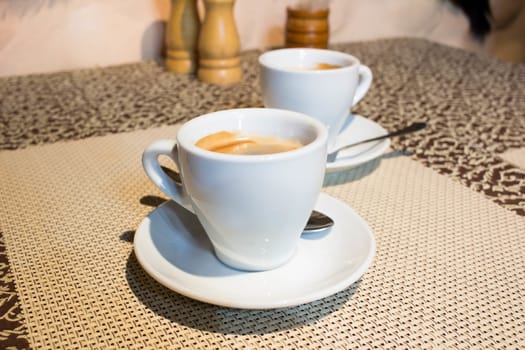 Composition of two cups of coffee on white serving plates with small metal spoons