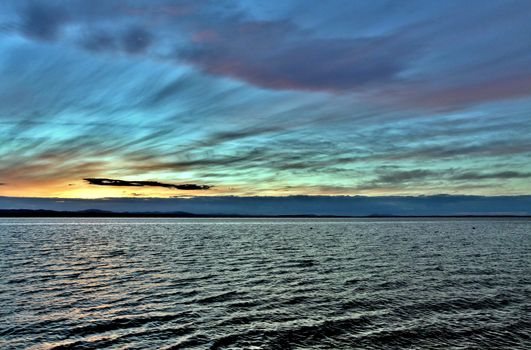 the evening sky over the lake, silhouettes of clouds illuminated by the sun, the sun sets over the horizon