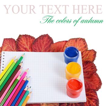 Colored pencils with notebook and autumn leaves