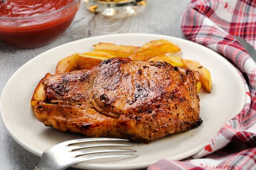 browned pork steak on a bone with fried potatoes.