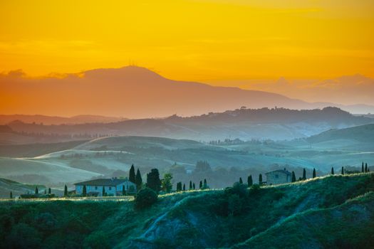 Evening in Tuscany. Hilly Tuscan landscape in golden mood at sunset time with silhouettes of cypresses and farm houses, Italy.
