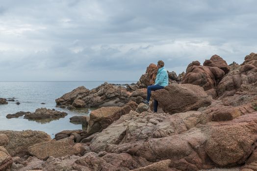 adult woman sitting on the rocks of isola rossa the read coast of sardinia island belongs to italy