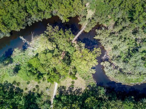 Timber bridge crosses a winding creek through gum tree forest.  Durras Creek Australia