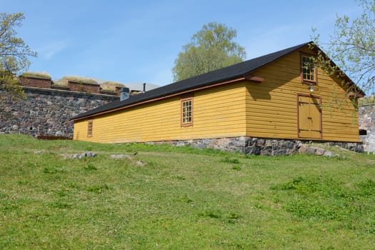 Yellow wooden hut with a black roof and stone foundations on a grassy patch on Suomenlinna island