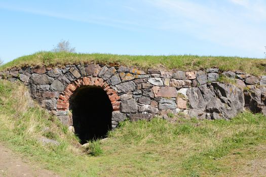 Dark tunnel entrance in a stone embankment in a grassy hillside. Copy space on blue sky above.