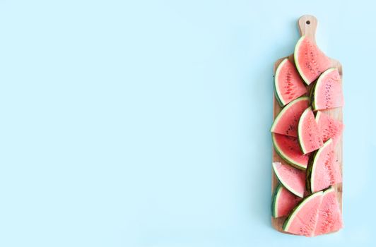 Fresh watermelon slices on chopping board on a blue background
