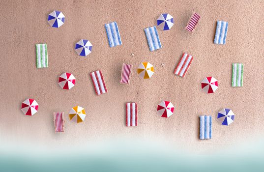 Miniature beach parasols and towels on sand 