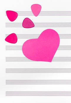 Pink heart and guitar picks on empty sheet music paper. Romantic music concept.