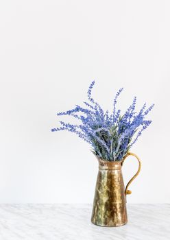Blooming blue lavender in antique metal jar, on marble surface.