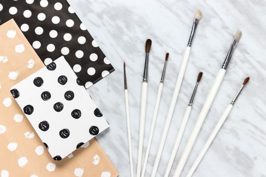 Paint brushes, decorative paper and notebook for artistic projects, on marble background.