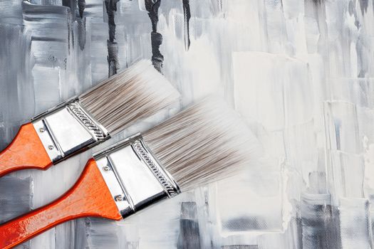 Two paint brushes on artistic canvas with black and white brush strokes.