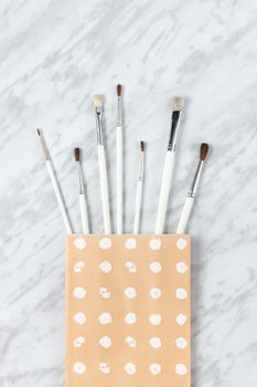 Paint brushes in a paper bag with white circles painted on it, on marble background.