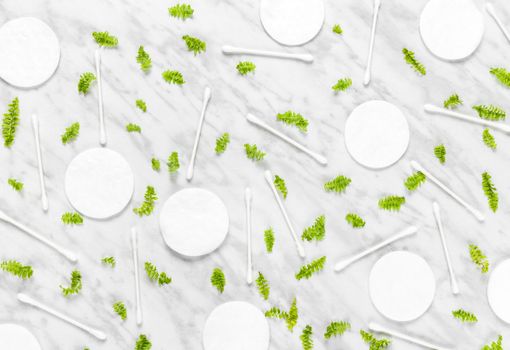 Cotton pads, Q-tips and green leaves on marble background. Flat lay composition.