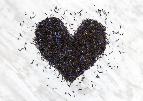 Heart made of black Earl gray tea leaves, on marble background. Tea love.