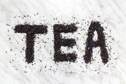The word "TEA" written with black Earl Gray tea leaves, on marble background.