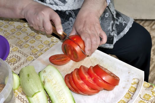 slicing tomatoes and zucchihi on the cutting Board, visible hands of the cook, cooking for the picnic