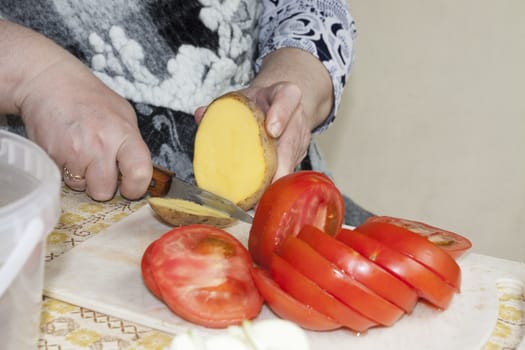 slicing potatoes and tomatoes on the cutting Board, visible hands of the cook, cooking for the picnic
