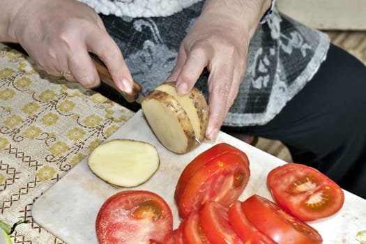 slicing potatoes and tomatoes on the cutting Board, visible hands of the cook, cooking for the picnic