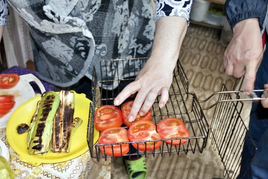 laying of fresh sliced tomatoes on the grate for roasting, visible hands of the cook, cooking for the picnic