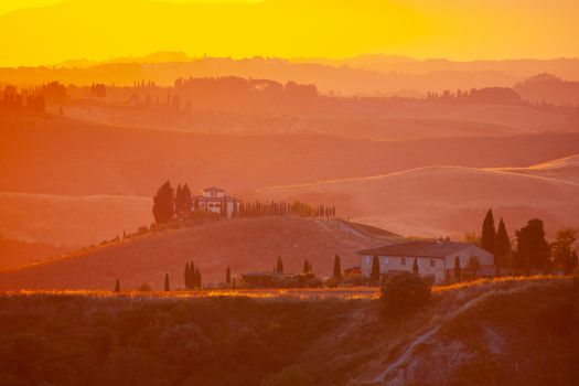 Evening in Tuscany. Hilly Tuscan landscape in golden mood at sunset time with silhouettes of cypresses and farm houses near Volterra, Italy.