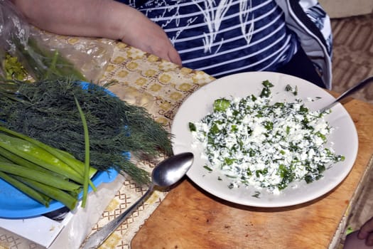 cottage cheese with greens in a plate, next to green onions, parsley, dill