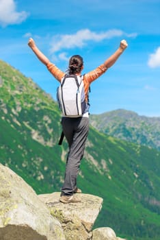 a happy tourist is standing near a cliff at the edge of a cliff with uplifted hands